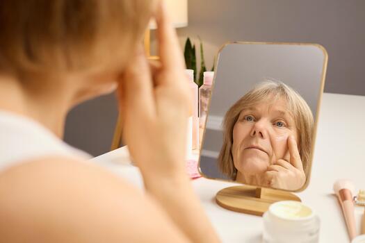 a-senior-woman-carefully-applies-skincare-cream-to-her-face-while-gazing-into-the-mirror-the-cozy-room-is-well-lit-creating-a-calming-atmosphere-for-her-morning-routine-photo